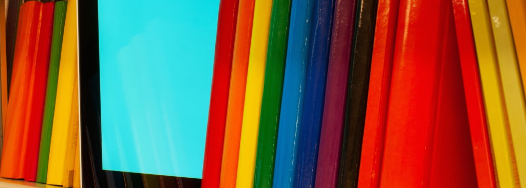 Row of colorful books and electronic book reader on the shelf